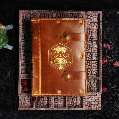 Handmade A5 leather adventure journal featuring a hand-gilded Hufflepuff badger crest, Marauder's Map footprints, and a wand duel spine design by Grimbeard Leather