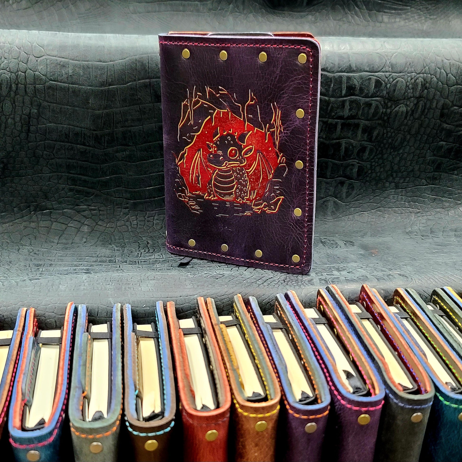Custom handmade leather pocket journal with hand-gilded baby dragon hatchling in a cave mouth design by Grimbeard Leather